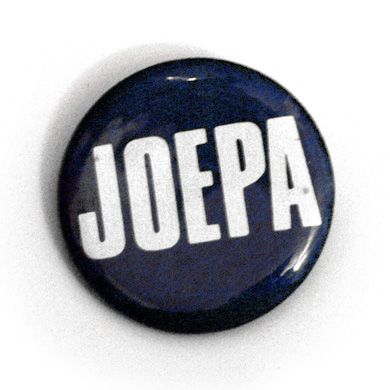 The respectable shorthand that everyone around State College, Pennsylvania, uses when they refer to the living legend, himself, Joe Paterno.  This is an old button of Candy's — she's wearing it to work today.  (2005)